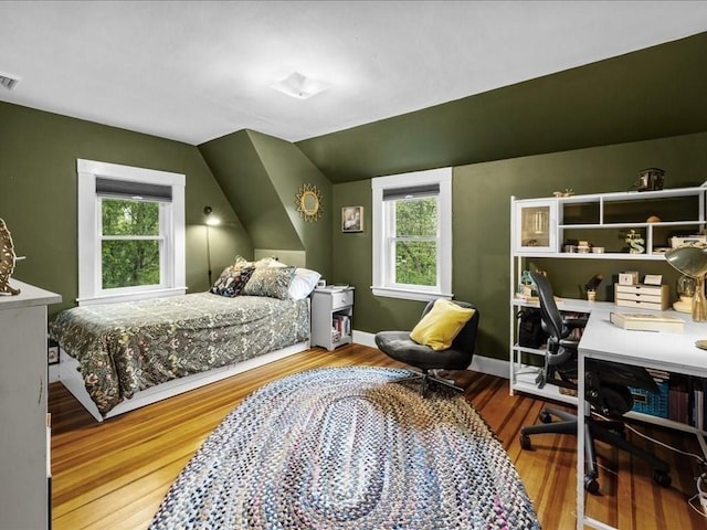 bedroom featuring wood finished floors, an office area, vaulted ceiling, and baseboards
