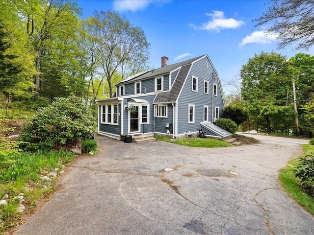 colonial inspired home featuring a chimney, asphalt driveway, a shingled roof, and a gambrel roof