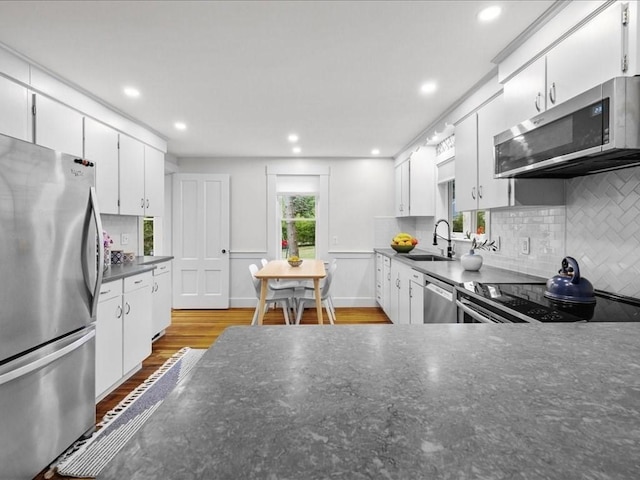 kitchen featuring appliances with stainless steel finishes, a sink, dark countertops, tasteful backsplash, and white cabinetry