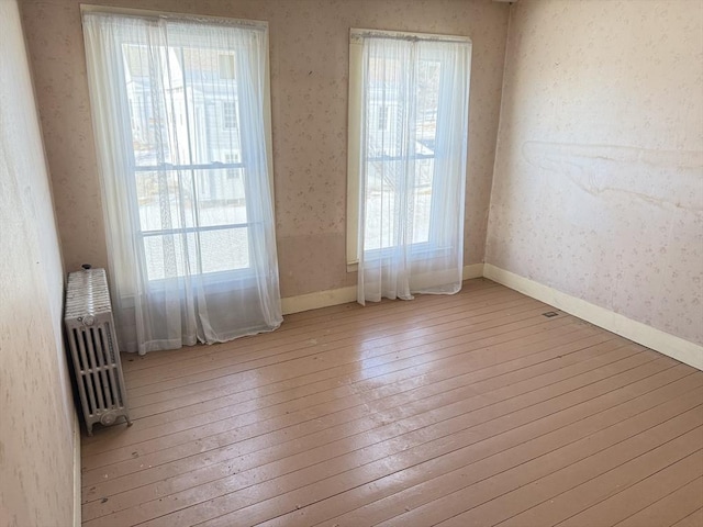 spare room with radiator heating unit and light hardwood / wood-style floors