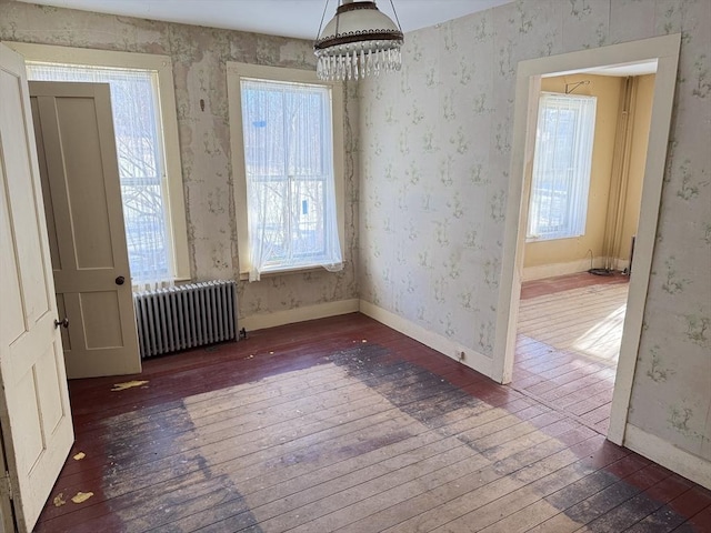 unfurnished room with dark wood-type flooring, radiator heating unit, and an inviting chandelier