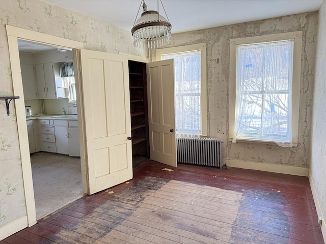 unfurnished dining area featuring a healthy amount of sunlight, radiator heating unit, and dark hardwood / wood-style floors