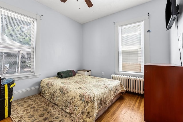 bedroom featuring radiator, wood-type flooring, baseboards, and ceiling fan