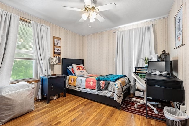 bedroom with wallpapered walls, wood finished floors, and ceiling fan