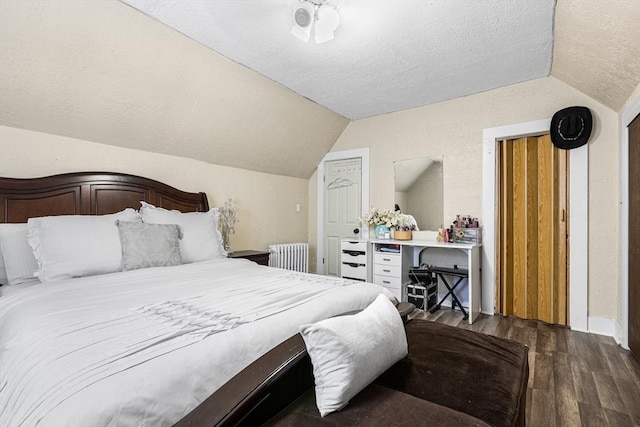 bedroom with radiator, vaulted ceiling, wood finished floors, a textured ceiling, and multiple closets