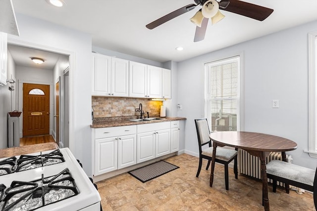kitchen with a sink, white gas range oven, tasteful backsplash, white cabinetry, and ceiling fan
