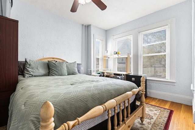 bedroom featuring a textured wall, wood finished floors, baseboards, and ceiling fan