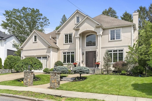 22 Scotney, Newton, MA 02467 - view of front facade featuring stucco siding, a chimney, a front yard, driveway, and roof with shingles