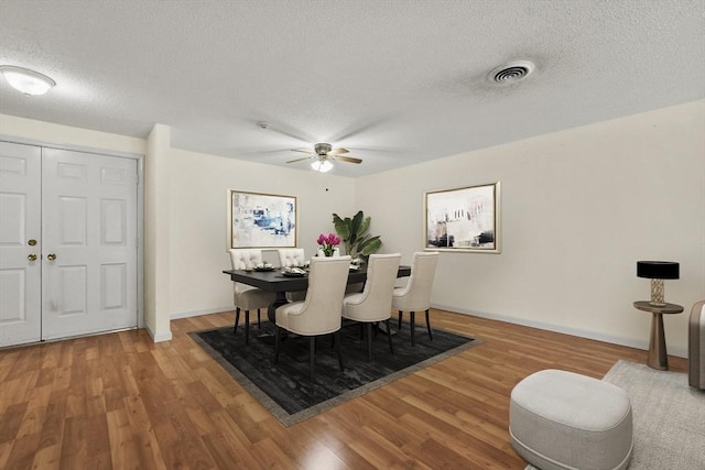 dining room featuring a textured ceiling, wood finished floors, visible vents, and baseboards