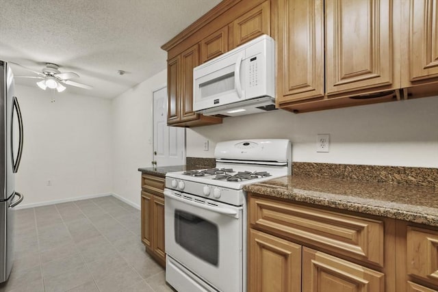 kitchen with dark stone counters, white appliances, a textured ceiling, and a ceiling fan