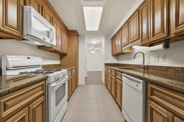 kitchen featuring brown cabinetry, dark stone counters, white appliances, and a sink