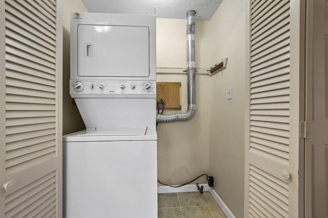 laundry area with light tile patterned floors, laundry area, baseboards, stacked washer and clothes dryer, and a textured ceiling