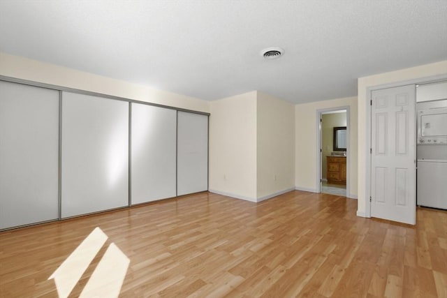 unfurnished bedroom with stacked washer and clothes dryer, visible vents, light wood-style flooring, and baseboards