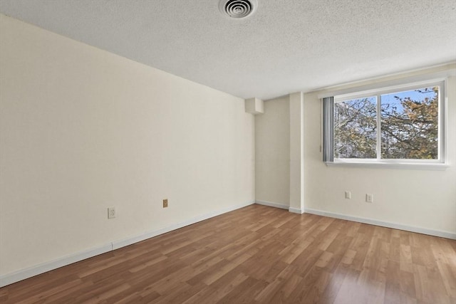 spare room featuring visible vents, a textured ceiling, baseboards, and wood finished floors