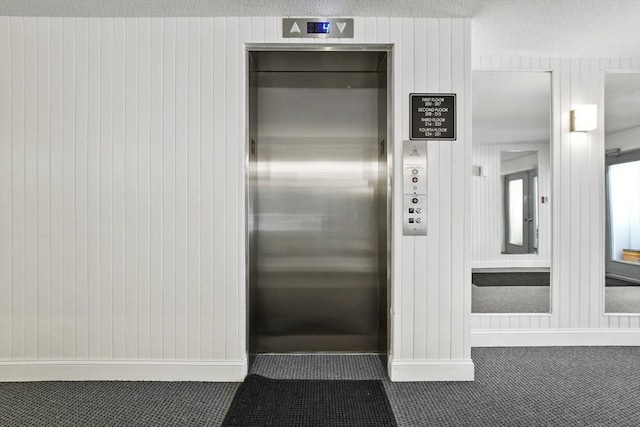 room details with elevator, wooden walls, a textured ceiling, and carpet flooring