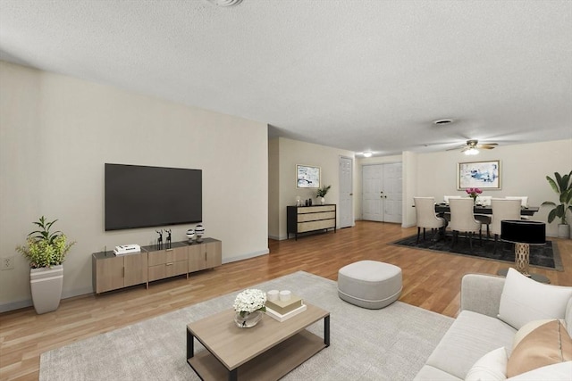 living area with baseboards, a textured ceiling, a ceiling fan, and wood finished floors