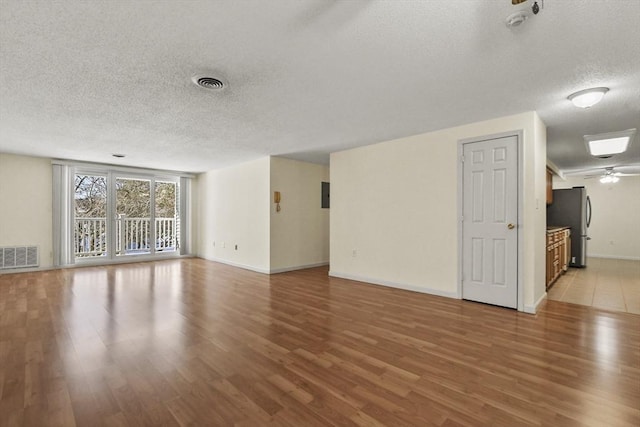 unfurnished living room with baseboards, a textured ceiling, visible vents, and wood finished floors