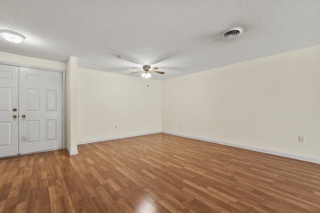 empty room with baseboards, visible vents, ceiling fan, wood finished floors, and a textured ceiling