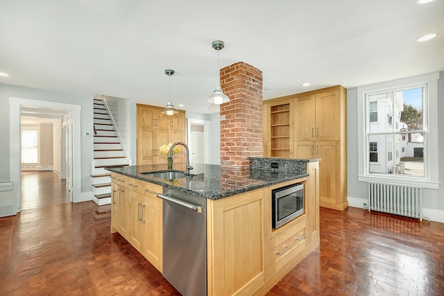 kitchen with radiator, decorative light fixtures, stainless steel appliances, a kitchen island with sink, and sink