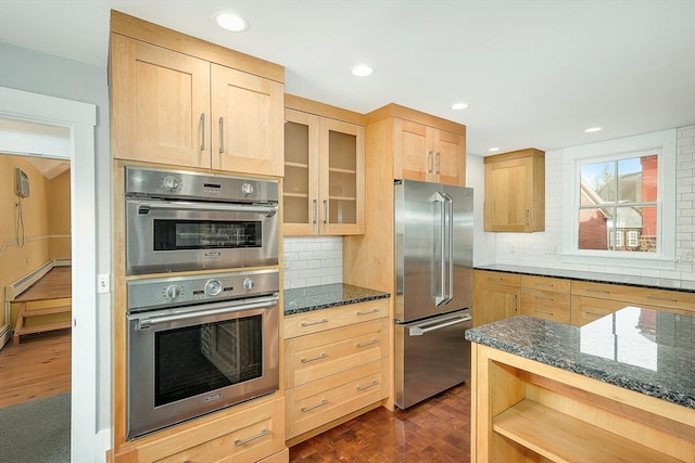 kitchen with light brown cabinets, backsplash, dark wood-type flooring, stainless steel appliances, and dark stone countertops