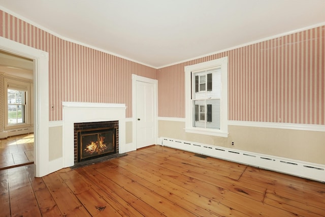 unfurnished living room with a baseboard heating unit, hardwood / wood-style flooring, and a brick fireplace