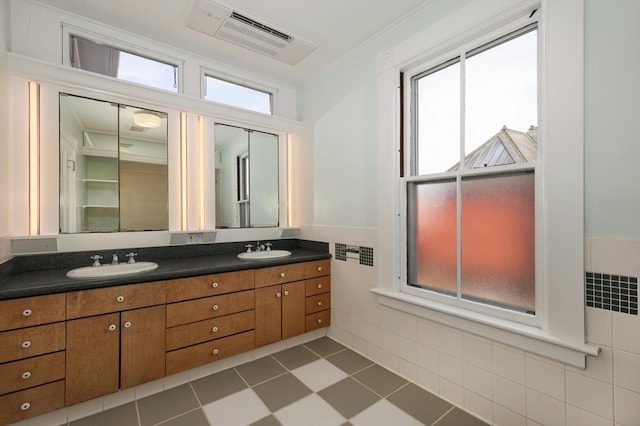 bathroom with ornamental molding, dual bowl vanity, tile floors, and tile walls