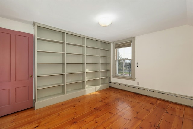 spare room with light wood-type flooring, built in shelves, and a baseboard heating unit