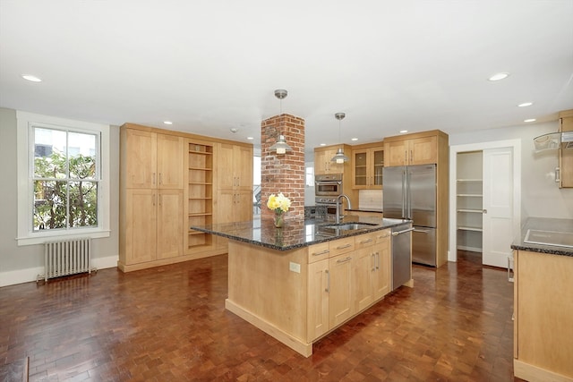 kitchen with a kitchen island with sink, radiator heating unit, sink, stainless steel appliances, and pendant lighting