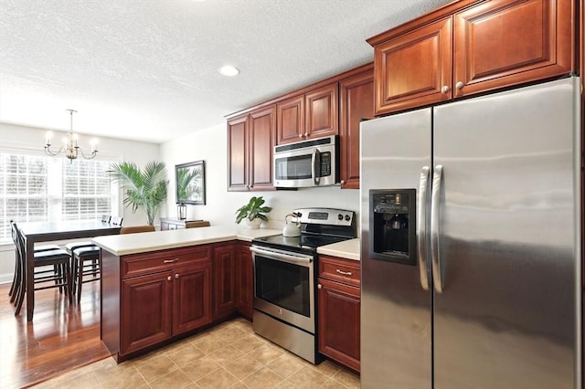 kitchen featuring a chandelier, light countertops, appliances with stainless steel finishes, a peninsula, and a textured ceiling