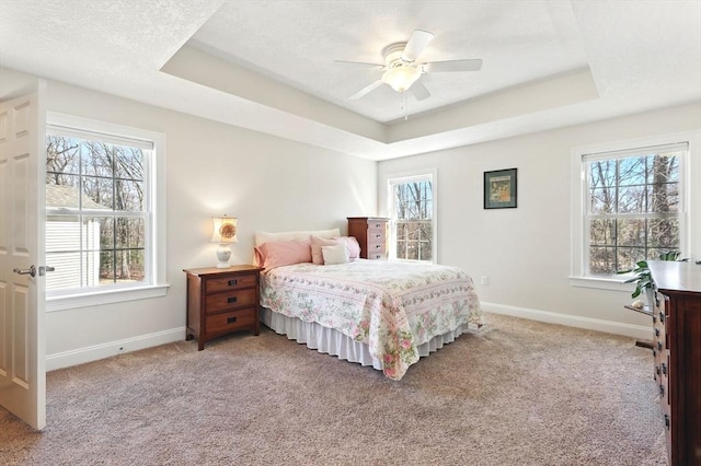 bedroom with a tray ceiling, multiple windows, and baseboards