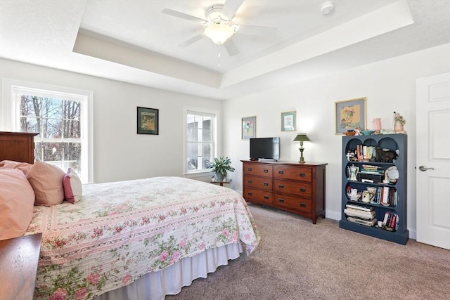 bedroom with light carpet, baseboards, a raised ceiling, and a ceiling fan