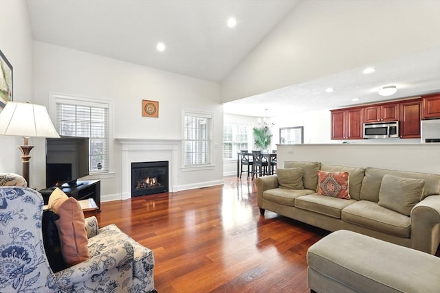 living room featuring dark wood-type flooring, high vaulted ceiling, a glass covered fireplace, recessed lighting, and baseboards