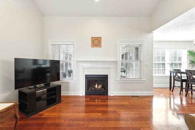 living area with a glass covered fireplace, visible vents, baseboards, and wood finished floors