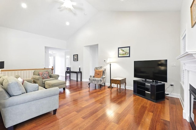 living area with a glass covered fireplace, high vaulted ceiling, baseboards, and wood finished floors