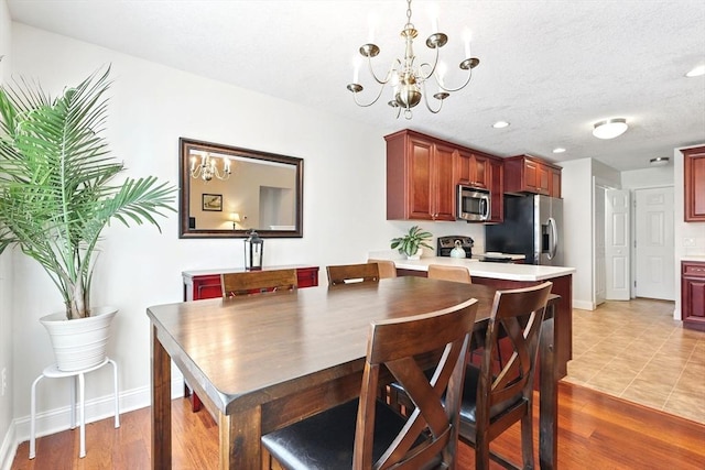 dining area with a notable chandelier, baseboards, light wood finished floors, and a textured ceiling