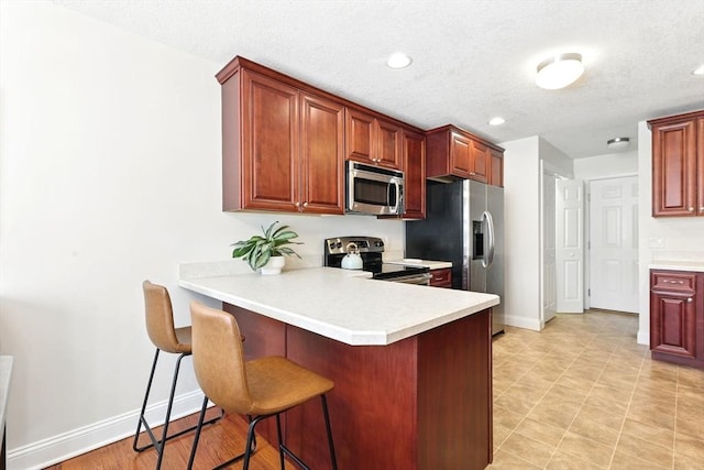 kitchen with a breakfast bar, stainless steel appliances, a peninsula, light countertops, and baseboards