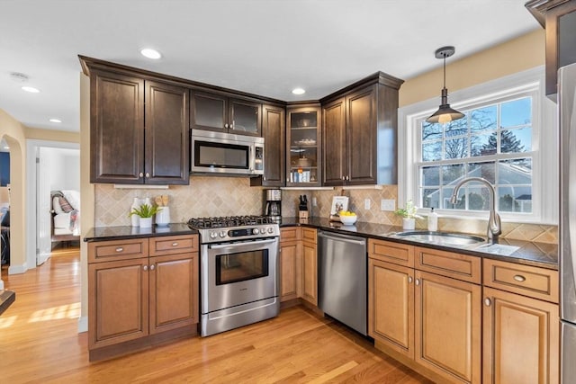 kitchen with sink, hanging light fixtures, stainless steel appliances, tasteful backsplash, and light wood-type flooring