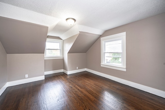 additional living space with lofted ceiling, dark wood-type flooring, and a textured ceiling