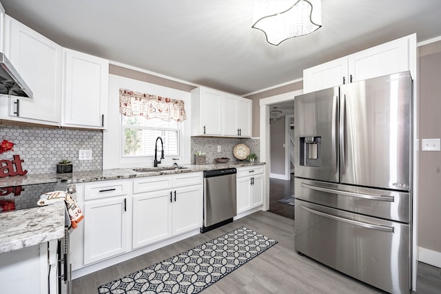 kitchen featuring decorative backsplash, appliances with stainless steel finishes, white cabinetry, light wood-type flooring, and light stone counters