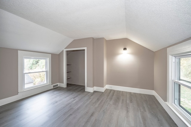 additional living space with a textured ceiling, light wood-type flooring, and vaulted ceiling