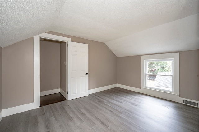 bonus room with lofted ceiling, hardwood / wood-style floors, and a textured ceiling