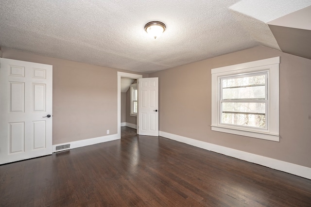 interior space with dark wood-type flooring, vaulted ceiling, and a textured ceiling