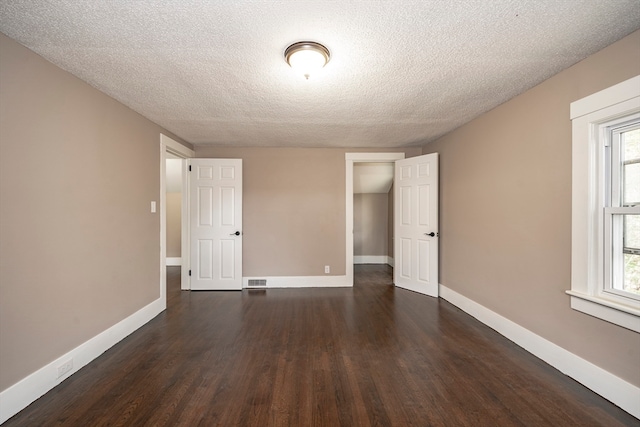 unfurnished bedroom with multiple windows, a textured ceiling, and dark wood-type flooring