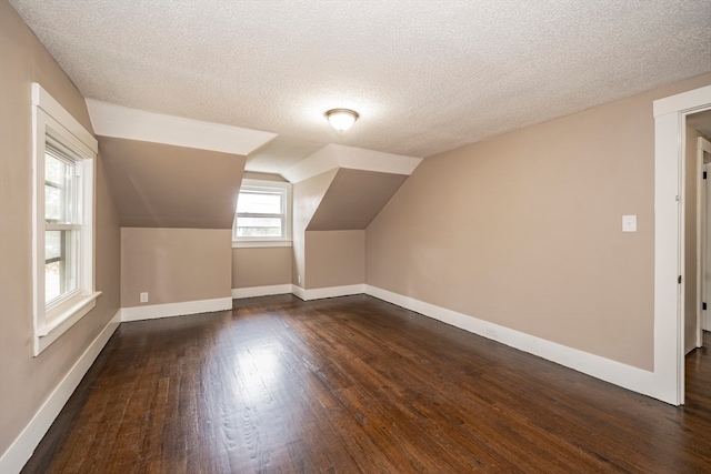 additional living space featuring dark wood-type flooring, a textured ceiling, and lofted ceiling