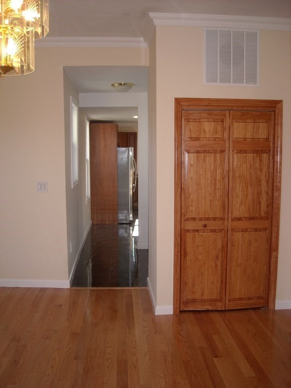 hall with wood-type flooring, crown molding, and a chandelier