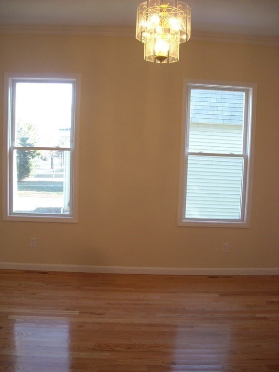 spare room featuring wood-type flooring, ornamental molding, and an inviting chandelier