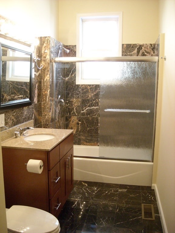 full bathroom with a wealth of natural light, combined bath / shower with glass door, vanity, and toilet