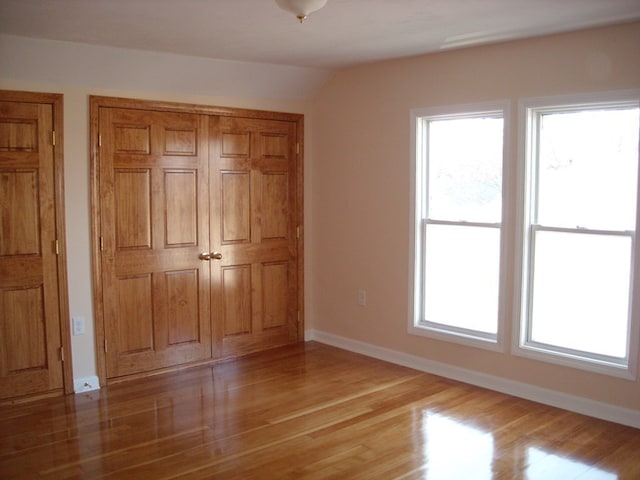 unfurnished bedroom with vaulted ceiling, light hardwood / wood-style flooring, and multiple windows