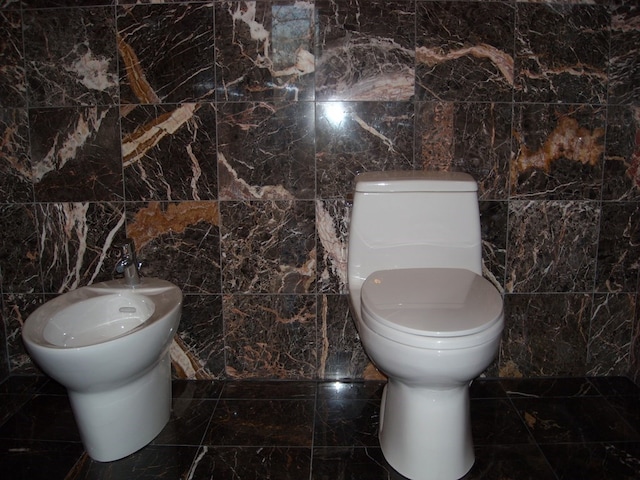 bathroom featuring toilet, a bidet, and tile walls