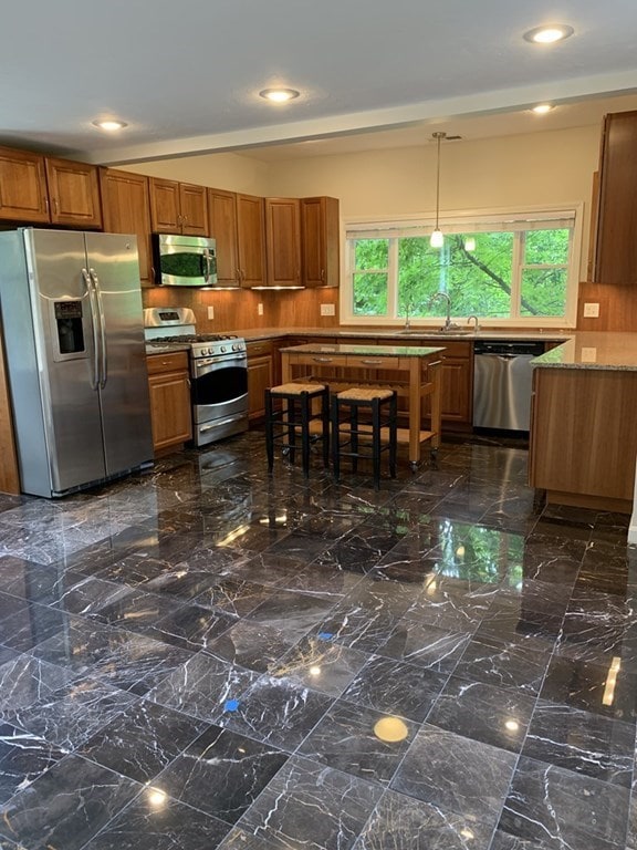 kitchen featuring appliances with stainless steel finishes, pendant lighting, light stone counters, and sink